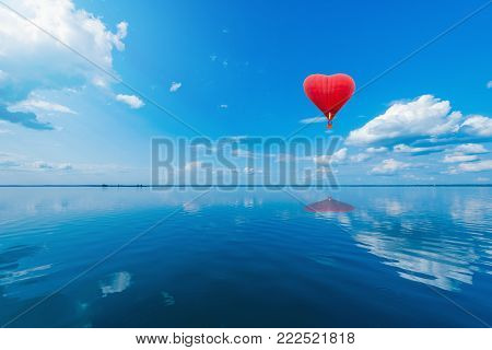 Red hot air balloon in the shape of a heart above the lake surface at windless weather time. Present trip on Valentine's Day.