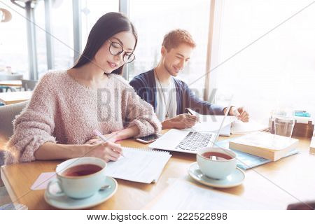 We are colleagues. Two colleagues sitting next to each other and leaning elbows on the table while being positive