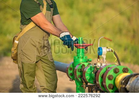 Oil Worker Is Turning Valve On The Oil Pipeline, Oil Deposit On The Background.