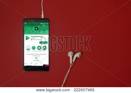 Los Angeles, January 11, 2018: Smartphone with Google play games application in google play store on red background with earphones plugged in and copy space