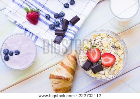 Romantic French or Rural Breakfast concept with youghurt, milk, muesli, croissant, fresh berries and chocolate. Colored wood and a plaid napkin as a background.