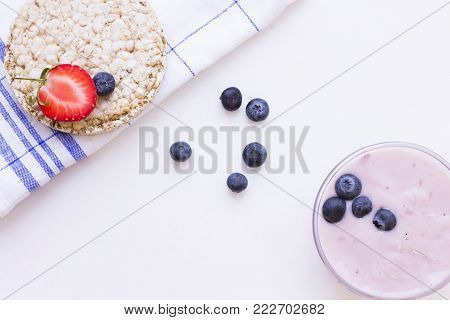 Healthy Breakfast Concept with wheat breadcrisp on a napkin, fresh blueberries and strawberries and homemade youghurt on white, top view, copy space