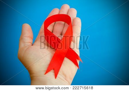 Red folded ribbon in hand on a blue background as a symbol of hemophilia