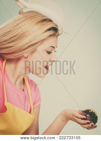 Diet, sweets, food concept. Woman holding delicious chocolate cupcake with peanut frosting about to take bite