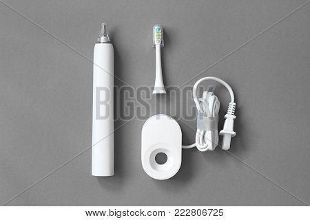 White electric toothbrush, cleaning brush and charger on a gray background. The concept of good mouth hygiene. Top view, flat lay.