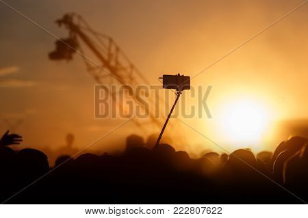 Smartphone on self-stick vs Television Camera hanging on crane, sunset time
