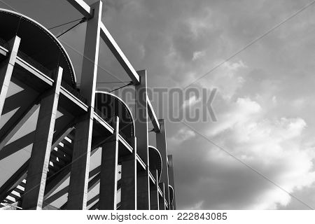 High architectonic vertical lines of a contemporaneous building (a sport arena) on a background of clouds the light filtered by clouds. A dynamic black & white image that makes us feeling small.