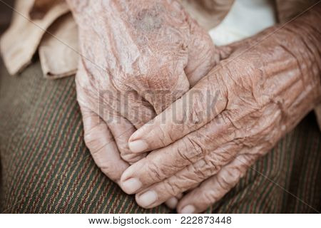 Hands Asian elderly woman grasps her hand on lap, pair of elderly wrinkled hands in prayer sitting alone in his house, World Kindness older and Adult care,  Mother day people concept