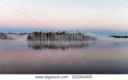 island on a forest lake in the fog at dawn
