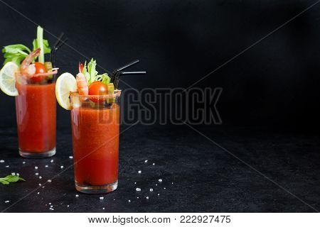 Bloody Mary Cocktail in glass with garnishes. Tomato Bloody Mary spicy drink on black background with copy space.