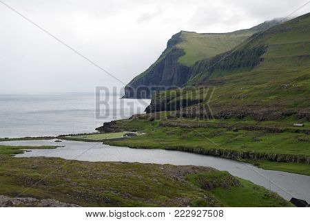 Green and high fjords near the town Eidi on Faroe Islands.
On the coast is a soccer pitch.