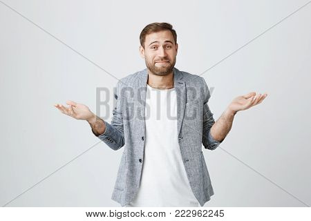 So what, Who cares. Unsure doubtful stylish european bearded man wearing jacket shrugging his shoulders in questioning gesture of uncertainty and having regretful clueless look