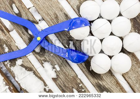 Blue plastic snowball maker tool with set of ready snowballs laying on a wooden bench near outdoor children playground at winter day.