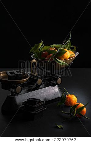 A bunch of fresh juicy clementines with green leaves in a scalepan and on a black table