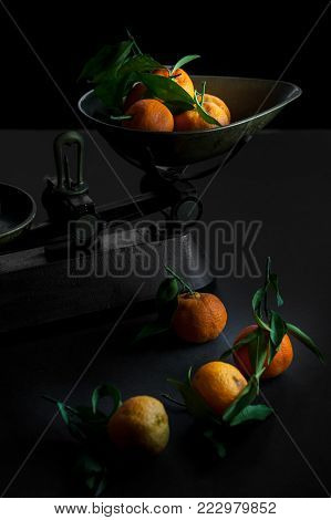 A bunch of fresh juicy clementines with green leaves in a scalepan and on a black table