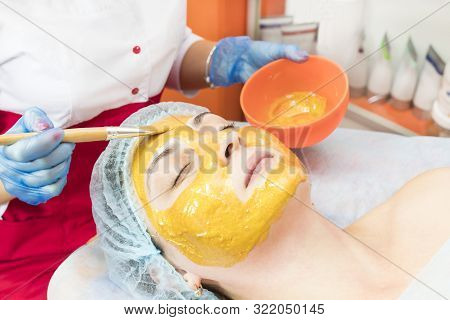 The Procedure In The Beauty Salon Applying A Personal Mask On The Face Of A Woman With A Mask Of Com