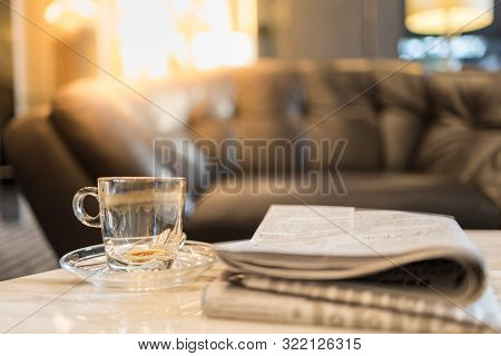 Close Up Of Empty And Drity Glass Cup Of Hot Coffee With Plate On Table With Newspaper In The Living