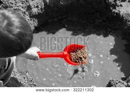 A Child Plays With A Red Dustpan And Basket On The Sandy Beach.