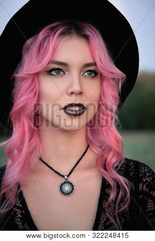 Halloween Theme: Beautiful Young Pink-haired Witch In Black Dress And Hat. Close-up Portrait