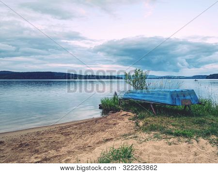 Lonely Fishing Vessel Boat Docked On Beach At Calm Lake. Laminate Or Wooden Fishing Boat In A Still 