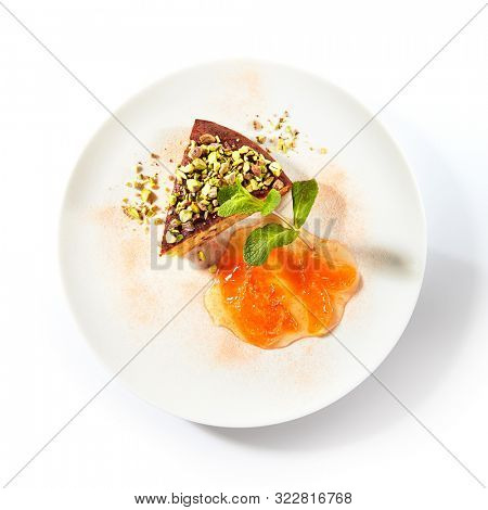 Healthy nut cake with apricot jam isolated on white background. Slice of walnut carrot sponge cake decorated with pistachios and fruit confiture on white round plate for restaurant menu top view