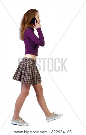 side view of a woman walking with a mobile phone. beautiful curly girl in motion.  Rear view people collection. Isolated over white background. red-haired girl in a skirt passes by talking on a smartp