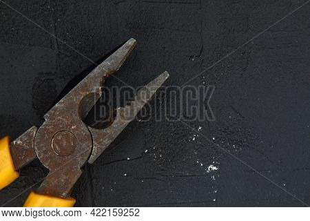 Pliers With A Yellow Handle On A Black Stone Background. Pliers, Nippers Isolated On Black. Open Met