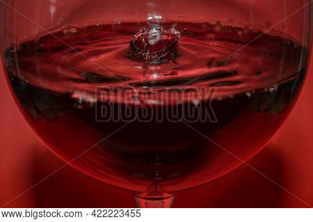 Redwine Drop In A Redwine Glass And Waves With Red Background And Reflection