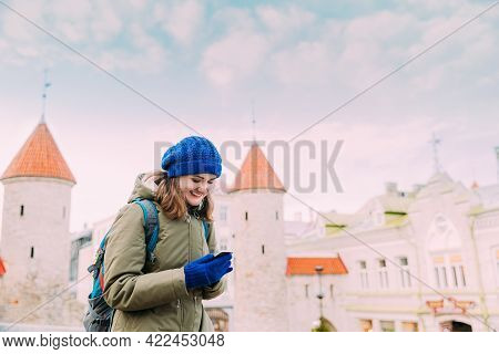 Tallinn, Estonia. Young Caucasian Woman Backpacker Tourist Enjoying Life, Smiling And Using Smartpho