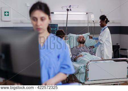 Black Doctor Checking Hospitalized Sick Man Monitoring Sickness Symptom During Recovery Appointment 