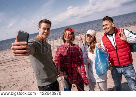 Happy Young Man Taking Selfie With Friends While Picking Up Trash.