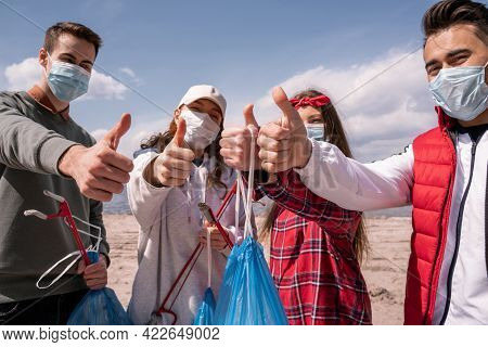 Young Volunteers In Medical Masks Holding Trash Bags And Grabbers While Showing Thumbs Up, Pick Up T