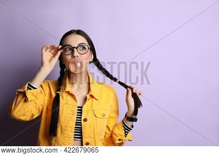 Fashionable Young Woman With Braids Blowing Bubblegum On Lilac Background, Space For Text