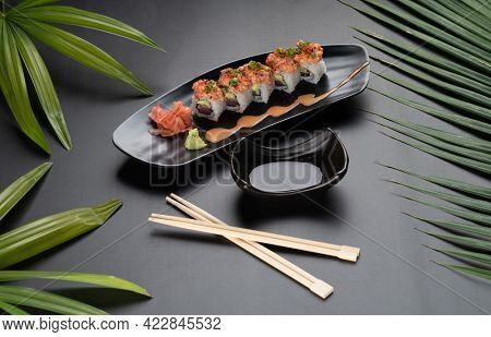 Sushi Roll - Maki Sushi made of tuna, avocado, mayonnaise and ebiko sushi isolated on black table with tropical leaves