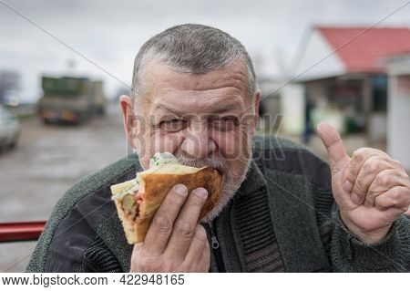 Portrait Of Hungry Caucasian Senior Driver Eating Lyulya Kebab In Lavash Near His Car