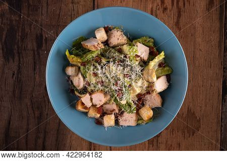Top view of chicken Cesar salad with croutons and grated cheese isolated on wooden rustic table