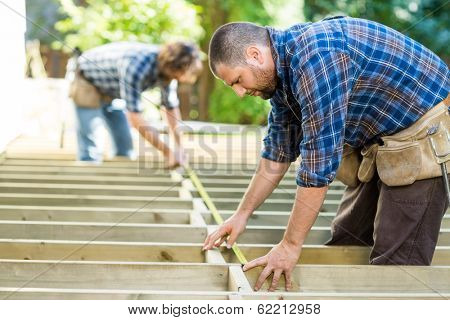 Mid adult carpenters measuring wood with tape at construction site