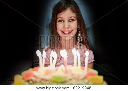 Portrait of little girl with birthday cake decorated by burning candles in semidarkness