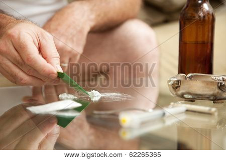 Man using powdered cocaine on a glass coffee table, with drug paraphanalia lying around.  