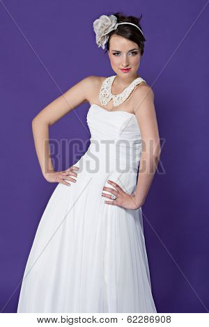 Beautiful young bride wearing white dresst and white lace collar with flower band on purple studio background 