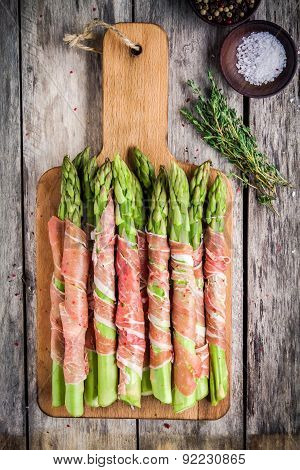 Fresh Organic Asparagus Wrapped In Parma Ham On A Cutting Board