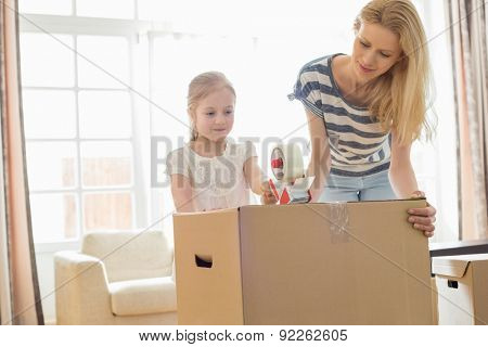 Mother and daughter packing cardboard box at home