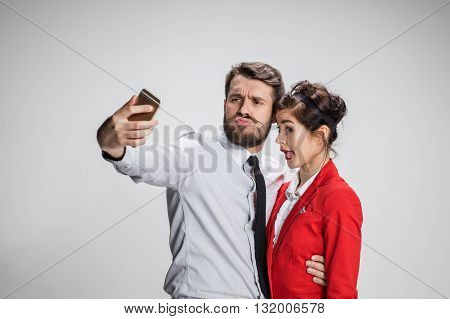 Two colleagues friends taking the picture to them self posing in the office, man and woman taking selfie with telephone camera, working funny in the office on gray background