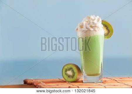 Kiwi smoothie set with sliced kiwi with sea on background. Cocktail made with kiwi and cream. Milkshake with fresh kiwi.