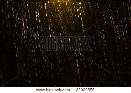 Night shot of a golden colored rain illuminated from the top by a lamp post with motion blur and droplets in focus and out of focus giving the sensation of depth. Can be used as a background pattern or texture and to convey emptiness solitude and loneline