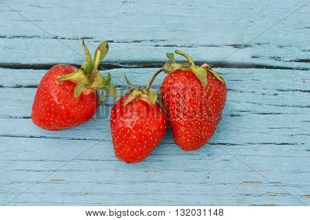three ripe juicy strawberries lying on a blue wooden table