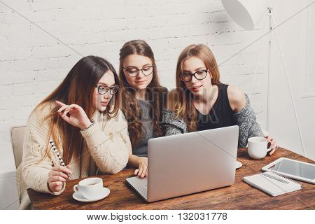 Three girls work and coffee with laptop. Young girls friends happy with computer. Discussion, startup, friendly conversation. Women friendship, modern life, gossip and internet dating concept.