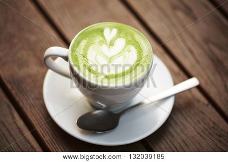 Cup of green tea matcha latte with latte art, standing on wooden table.