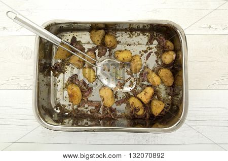 Mustard-crusted new potatoes with shallots in a dish with serving spoon on a rustic wooden table
