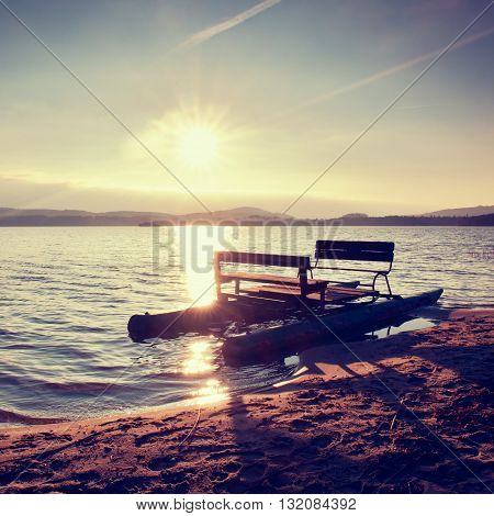 Abandoned old rusty pedal boat stuck on sand of beach. Wavy water level island on horizon. Autumn weather at coastline
